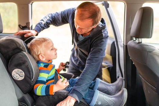 Father fastening safety belt for his baby boy in his car seat. Children's Car Seat Safety