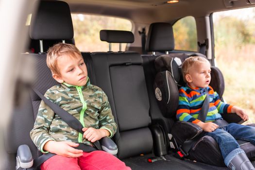 Two little boys sitting on a car seat and a booster seat buckled up in the car. Children's Car Seat Safety