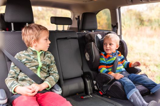 Two little boys sitting on a car seat and a booster seat buckled up in the car. Children's Car Seat Safety