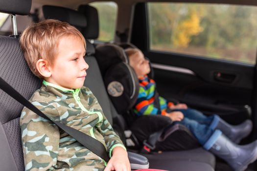 Two little boys sitting on a car seat and a booster seat buckled up in the car. Children's Car Seat Safety