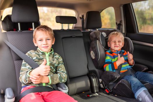 Two little boys sitting on a car seat and a booster seat buckled up in the car. Children's Car Seat Safety