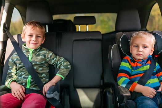 Two little boys sitting on a car seat and a booster seat buckled up in the car. Children's Car Seat Safety