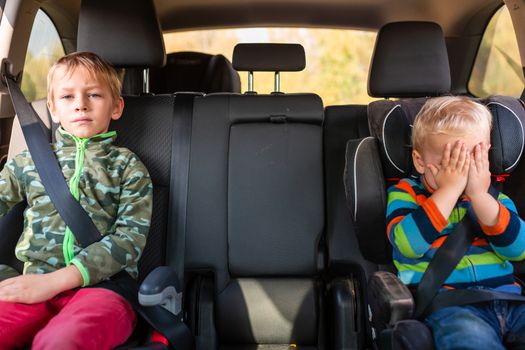 Two little boys sitting on a car seat and a booster seat buckled up in the car. Children's Car Seat Safety