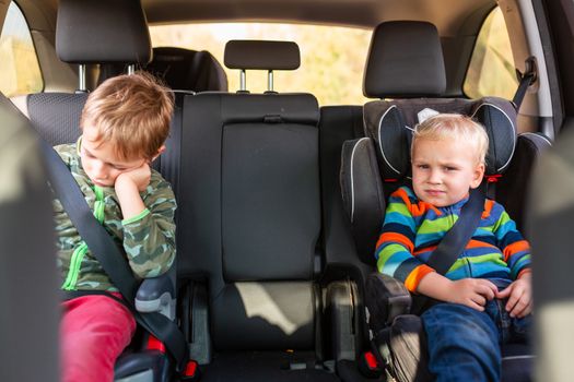 Two little boys sitting on a car seat and a booster seat buckled up in the car. Children's Car Seat Safety