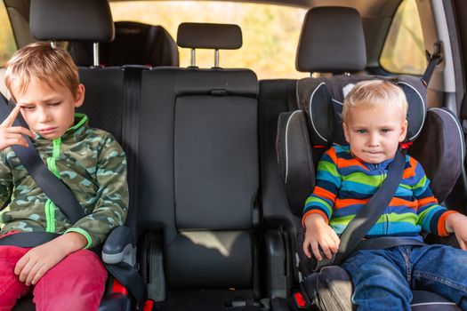 Two little boys sitting on a car seat and a booster seat buckled up in the car. Children's Car Seat Safety