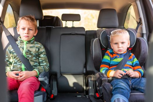 Two little boys sitting on a car seat and a booster seat buckled up in the car. Children's Car Seat Safety