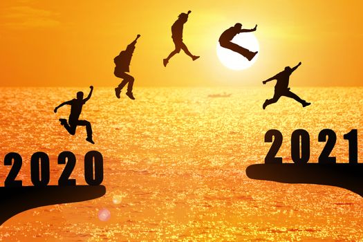 Silhouette group of young mans jumping between 2020 and 2021 years with beautiful sunset at the sea.