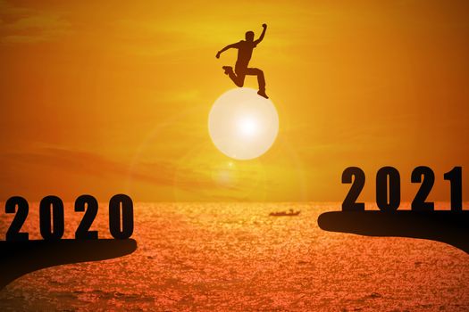 Silhouette of young man jumping between 2020 and 2021 years with beautiful sunset at the sea.