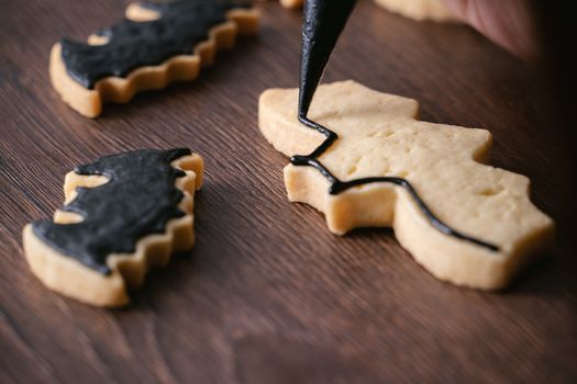 Close up of decorating cute Halloween bat gingerbread sugar cookies with frosting icing cream topping bag.