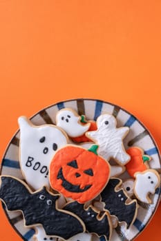 Top view of Halloween festive decorated icing gingerbread sugar cookies on orange background with copy space and flat lay layout.