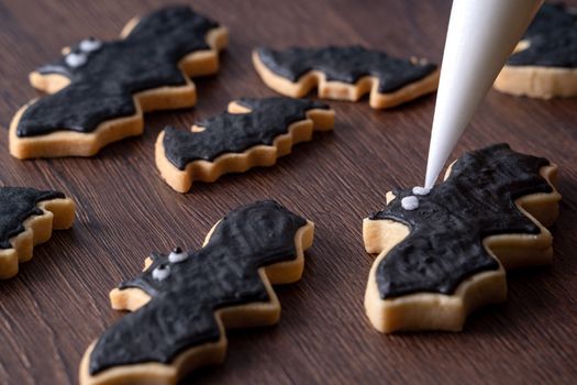 Close up of decorating cute Halloween bat gingerbread sugar cookies with frosting icing cream topping bag.