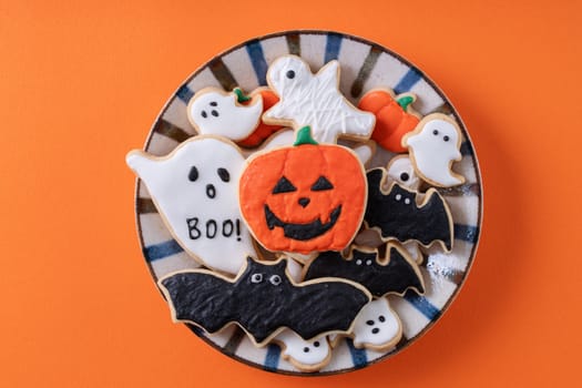 Top view of Halloween festive decorated icing gingerbread sugar cookies on orange background with copy space and flat lay layout.