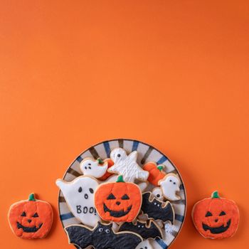 Top view of Halloween festive decorated icing gingerbread sugar cookies on orange background with copy space and flat lay layout.