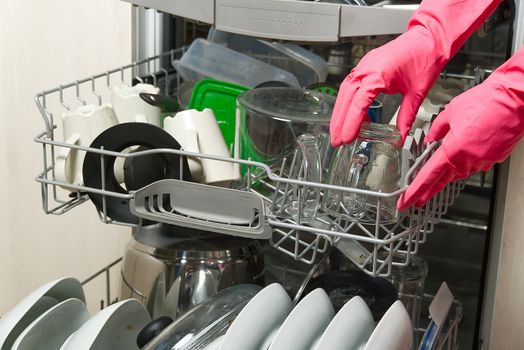Dirty dish in open integrated dishwasher. housewife hand putting dirty dishes to full loaded dishwasher. Open dishwasher with dirty dishes inside before washing. women hands in gloves placing plate for cleaning in machine