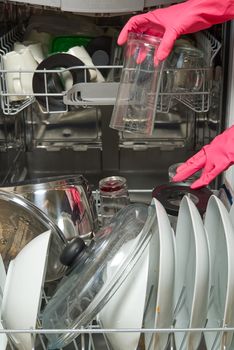 Dirty dish in open integrated dishwasher. housewife hand putting dirty dishes to full loaded dishwasher. Open dishwasher with dirty dishes inside before washing. women hands in gloves placing plate for cleaning in machine