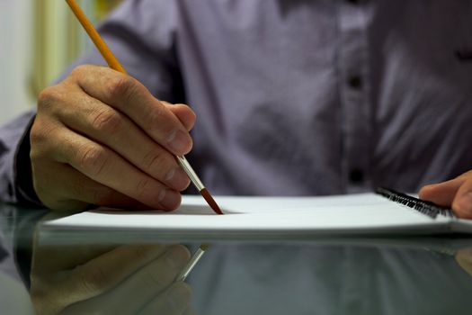 Hand holds paint Brush on paper of drawing book