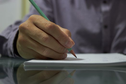 Hand holds pencil writing on  paper of notebook