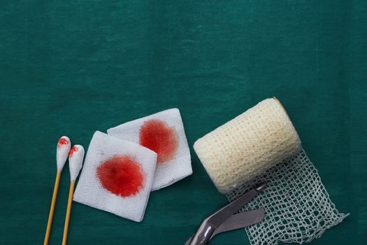 tools include scissors, swabs,net roll gauze and blood gauze on green surgical dress  for clean wound with copy space