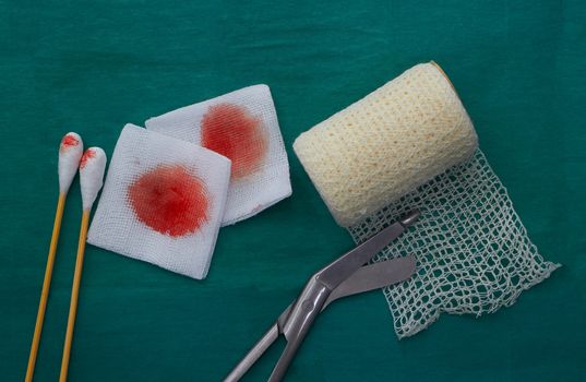 tools include scissors, swabs,net roll gauze and blood gauze on green surgical dress  for clean wound