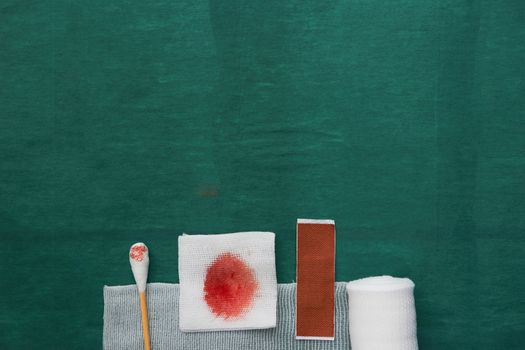 plaster,swab,blood gauze and roll gauze on green surgical dress for clean wound with copy space