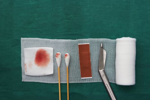 tools includes plaster,swab,blood gauze ,scissors and roll gauze on green surgical dress