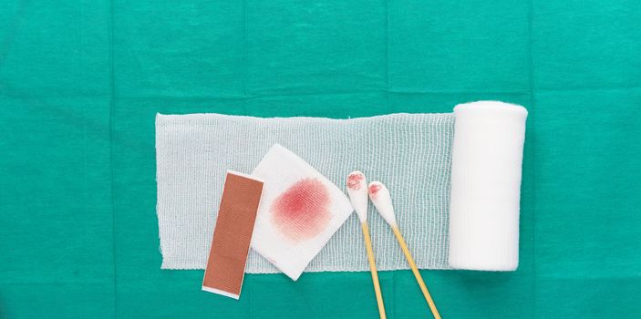roll gauze and swabs  and plaster and blooded gauze on green surgical medical background