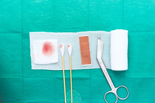 roll gauze and swabs and scissors and plaster and blooded gauze on green surgical medical background