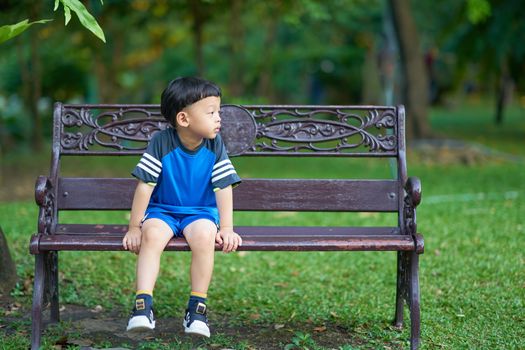 Thai boy sit on bench in park with green botany background