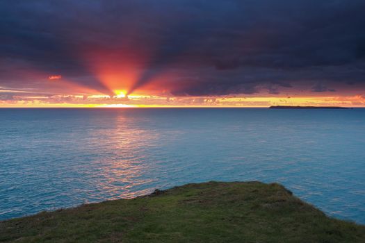 Amazing orange sunset lighting up dark clouds looking out from St. Anns Head over Skokholm island, south Pembrokeshire coast, Wales, UK