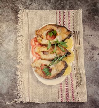 On the table on a plate pieces of fried carp with tomatoes and lemon. Top view, close-up