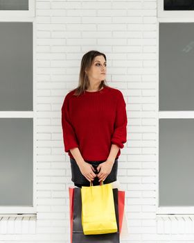 Adult woman with colorful shopping bags in front of a white brick wall