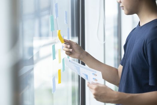 Young creative man reading sticky notes on glass wall.
