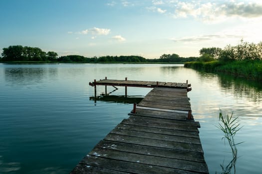 A wooden jetty on a calm lake and clouds on the blue sky