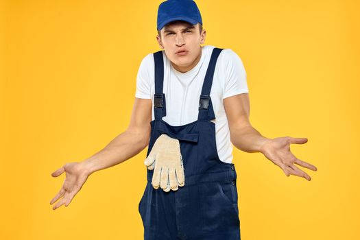 Working man in uniform of gloves rendering service yellow background. High quality photo