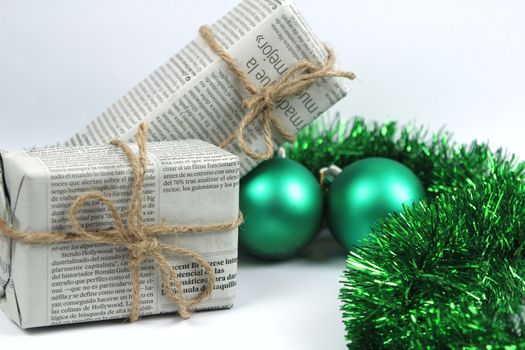 Gifts wrapped in old newspaper with green tinsel, rope and green baubles on white background