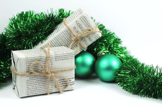 Gifts wrapped in old newspaper with green tinsel, rope and green baubles on white background