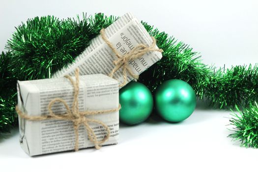 Gifts wrapped in old newspaper with green tinsel, rope and green baubles on white background