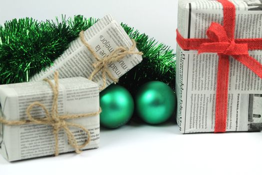 Gifts wrapped in old newspaper with green tinsel, rope and green baubles on white background