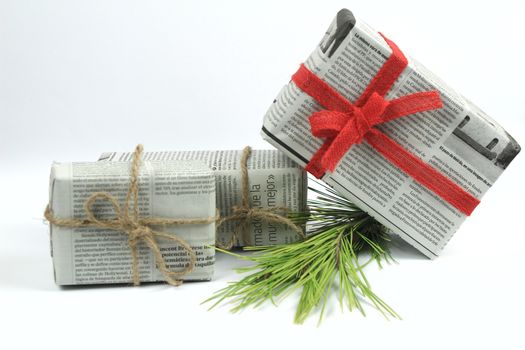 Gifts wrapped in old newspaper with pine branch, rope and green baubles on white background