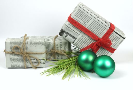 Gifts wrapped in old newspaper with pine branch, rope and green baubles on white background