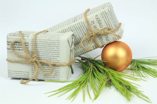 Gifts wrapped in old newspaper with pine branch, rope and golden bauble on white background