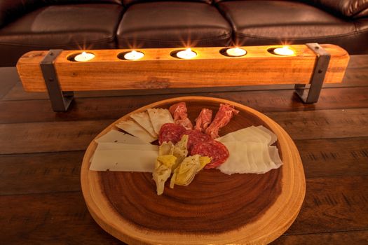 Charcuterie board on rustic wood with candles behind a spread of prosciutto, mozzarella cheese, Genoa salami, Fontina cheese and artisanal crackers.