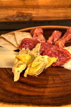 Charcuterie board on rustic wood with candles behind a spread of prosciutto, mozzarella cheese, Genoa salami, Fontina cheese and artisanal crackers.