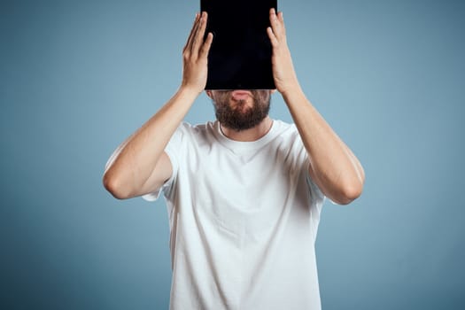 man with tablet near face on blue background cropped view touch monitor new technologies Copy Space. High quality photo