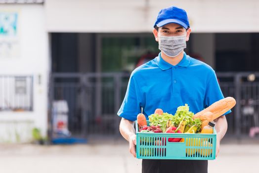 Asian grocery store delivery man wearing blue uniform and face mask protect he delivering fresh food vegetable in plastic box at door front home after coronavirus outbreak, back to new normal concept