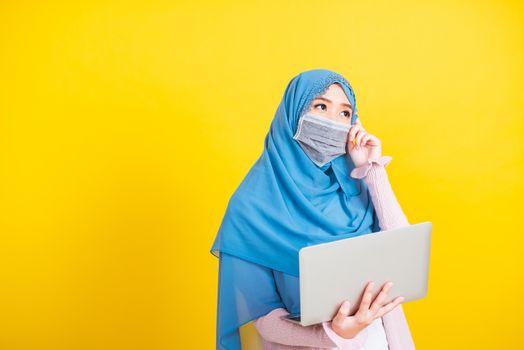 Asian Muslim Arab, Portrait of happy beautiful young woman Islam religious wear veil hijab and face mask protect she quarantines disease coronavirus hold laptop computer and thinking question