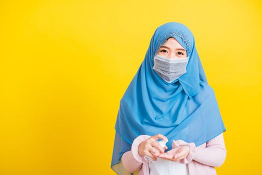 Asian Muslim Arab, Portrait of happy beautiful young woman Islam religious wear veil hijab and face mask protect she quarantines disease coronavirus apply alcohol spray to hands isolated yellow