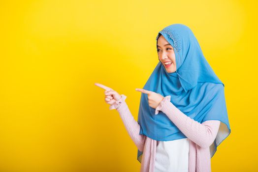 Asian Muslim Arab, Portrait of happy beautiful young woman Islam religious wear veil hijab funny smile she positive expression pointing finger side sideways to space isolated yellow background