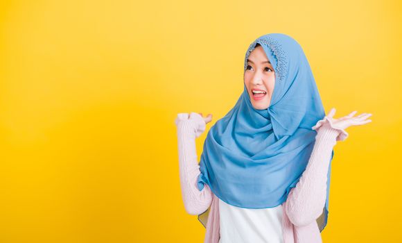 Asian Muslim Arab, Portrait of happy beautiful young woman Islam religious wear veil hijab funny smile she victories expression raises hands glad excited cheerful isolated yellow background
