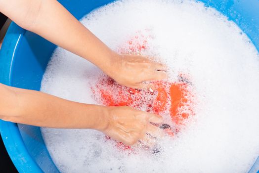 Closeup young Asian woman use hands washing color clothes in basin with detergent have soapy bubble water, studio shot background, laundry concept